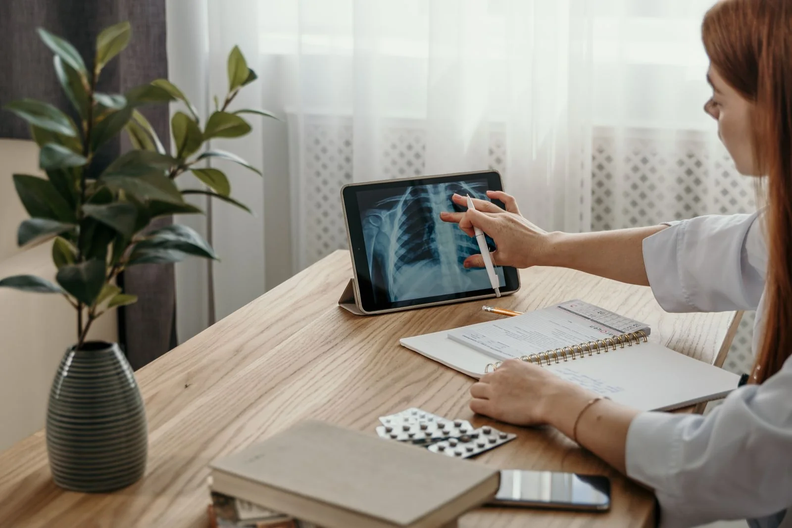 A doctor examining an X-ray on a tablet at a desk, her notes open beside it